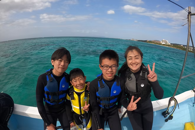 ガイドに見守られながら、子ども連れの家族が沖縄の海でシュノーケリングを楽しんでいる様子