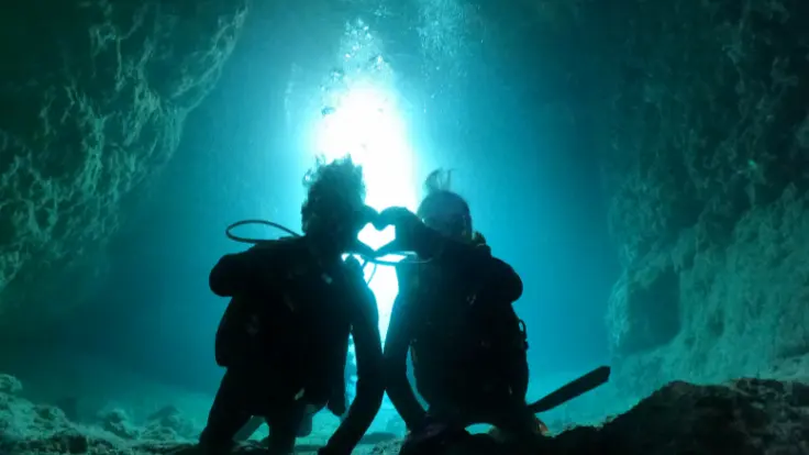 青の洞窟で体験ダイビングの記念撮影をする様子（水中の光を背に撮影）