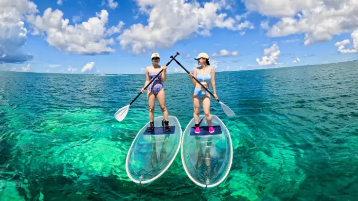 沖縄の海でクリアサップに乗る女性。透明なボードと青い海が映える体験イメージ