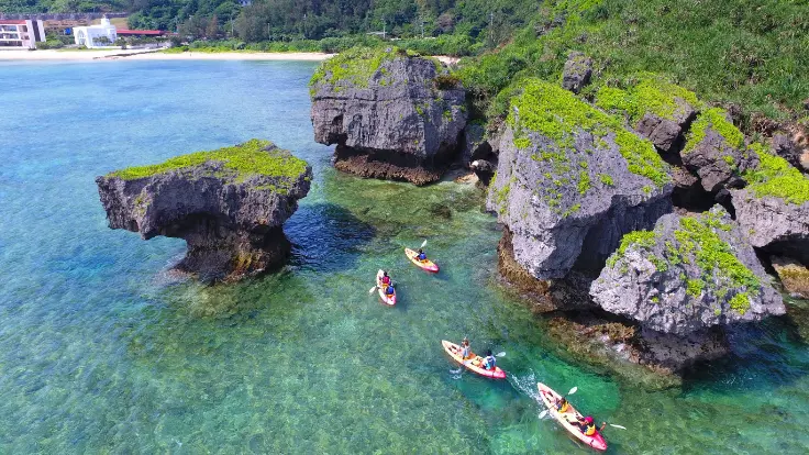 沖縄の海でカヤックを楽しむ様子。岩場の海岸線を眺めながら進むイメージ