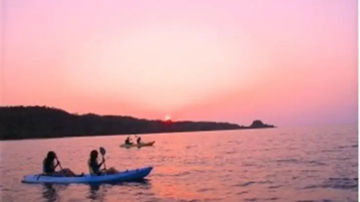 沖縄の夕暮れの海でサンセットカヤックを楽しむ様子。空がオレンジ色に染まり、水面にも光が映っているイメージ