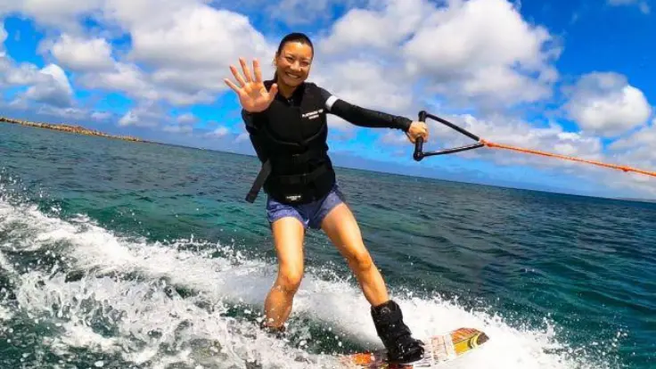 沖縄の海でウェイクボードを楽しんでいる様子。水面をすべるように進むマリンスポーツ体験イメージ。
