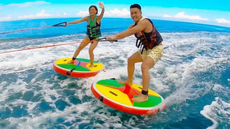 沖縄の海でディスクボードを楽しんでいる様子。座って乗りながら水面を走るマリンスポーツ体験イメージ。