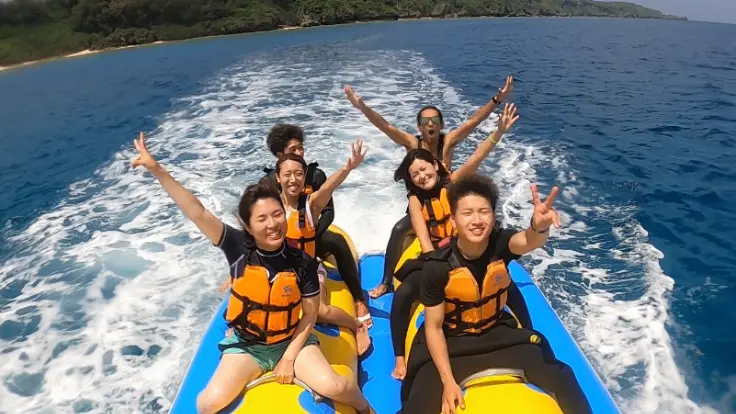 沖縄の海でバナナボートを楽しんでいる様子。海の上を走りながらスピード感を味わえるマリンスポーツ体験イメージ。