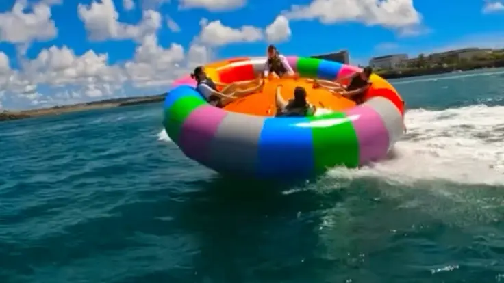 沖縄の海でハリケーンボートを楽しんでいる様子。大型の引き物に乗ってスリルを味わうマリンスポーツ体験イメージ。