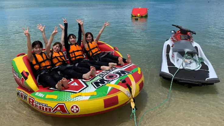 沖縄の海で座って楽しむマリンスポーツを体験している様子。海の上を走りながらスリルや開放感を味わえる体験イメージ。