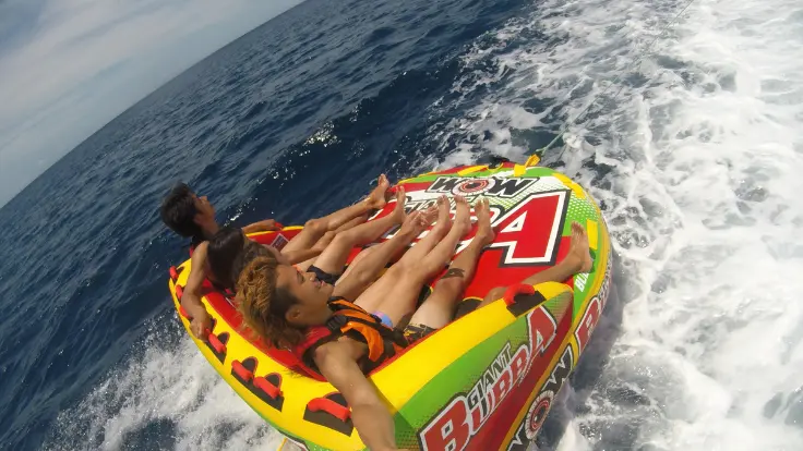 沖縄の海で家族でマーブル系のマリンスポーツを楽しんでいる様子。丸いチューブに乗って海の上を走っている体験イメージ。