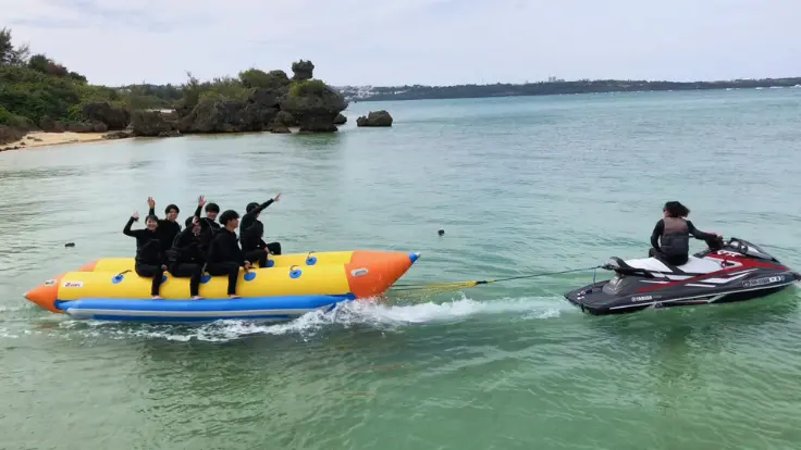 沖縄の海でみんなでチューブ系マリンスポーツを楽しんでいる様子。短時間でも一緒に盛り上がれる体験イメージ。
